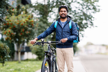 food shipping, profession and people concept - happy smiling indian delivery man in bike helmet with thermal insulated bag and bicycle on city street
