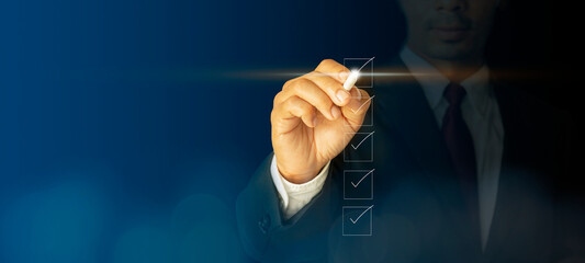 Checklist concept businessman checking mark on the checkboxes with marker white with a virtual screen, modern on dark blue background concept, can put your text at the pen, copy space