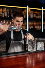 Bartender in apron adds ingredient to glass