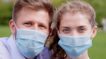 Bokeh close up shot of young couple wearing safety mask looking at camera outdoors