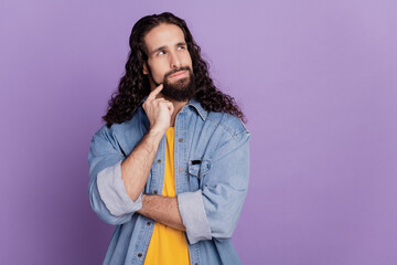 Portrait of handsome minded young man finger chin look up blank space on purple wall