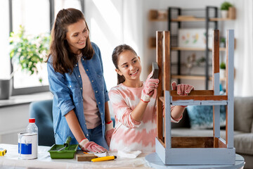 furniture renovation, diy and home improvement concept - happy smiling mother and daughter sanding old round wooden table with sponge at home