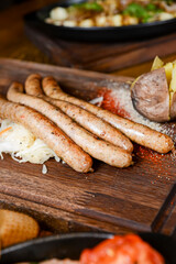 Stack of cooked sausages served on a rustic wooden board with sauce and baked potatoes.