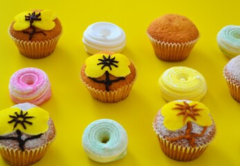 Rows of muffins decorated with powdered sugar and yellow flower shaped icing on a yellow background