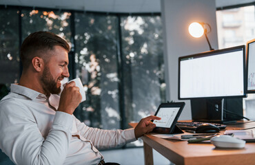 Busy day. Young businessman in formal clothes is in office with multiple screens