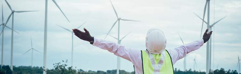 African male engineers working on site with wind turbine propeller and clear blue sky on the...