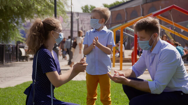 Young family in safety mask using antiseptic gel to disinfect hands outdoors
