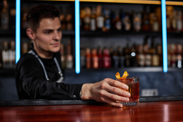 Barman holding out glass with alcoholic cocktail to the client
