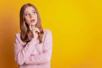 Photo of minded intelligent girl finger chin look up empty space on yellow background