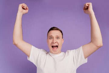 Fototapeta premium Portrait of positive crazy screaming man raise fists open mouth on violet background