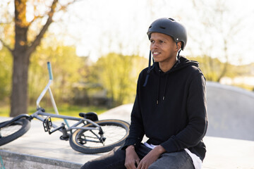 A boy came to the skatepark and sits on the ramp with his bike because he is afraid to go on the...