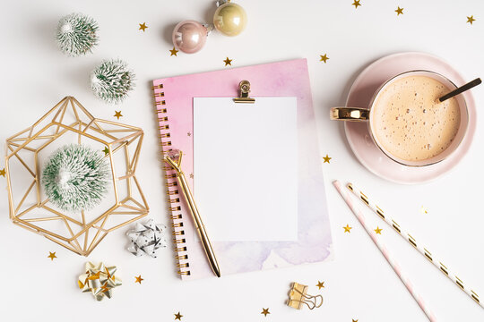 Desktop blank note pad. Flat lay of white working table background with cup of coffee and Christmas decoration. Top view balls, fir tree, paper clips, mock up greeting card, craft Notebook and pen.