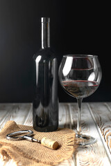 Wine glass and Bottle on a wooden table over black background. Alcoholic drink in a bottle and tall...
