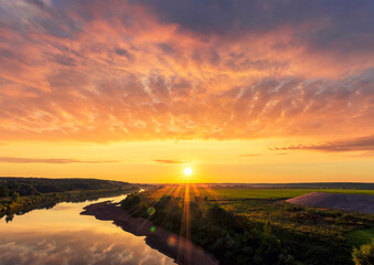 amazing view at beautiful summer river sunset, halo with reflection on water with green bushes, calm water ,deep colorful cloudy sky and glow on horizon on a background, spring evening landscape