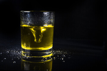 glass of watA glass of thin transparent glass with a yellow liquid swirling in a vortex, on a dark background with water drops at the baseer on black background