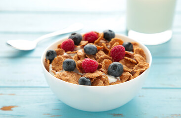 Breakfast with corn flakes, milk and berry on blue background.