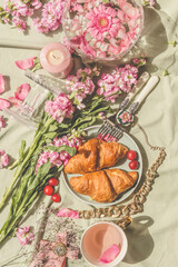 Sunny aesthetic picnic with croissants, pink flowers bunch, rose petal and tea cup. French breakfast. Outdoor. Top view
