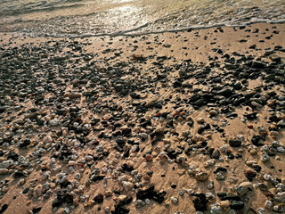 Pebbles on a beach in Africa. Small black, gray stones on a sand. Coastline of Atlantic Ocean, Cape Verde. Selective focus on the details, blurred background.