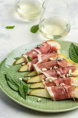 Appetizer with pear, blue cheese, prosciutto ham and basil. Italian antipasto with white wine, top view