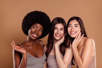 Photo of dreamy fancy three best friends wear cropped tops smiling hugging looking empty space isolated beige color background