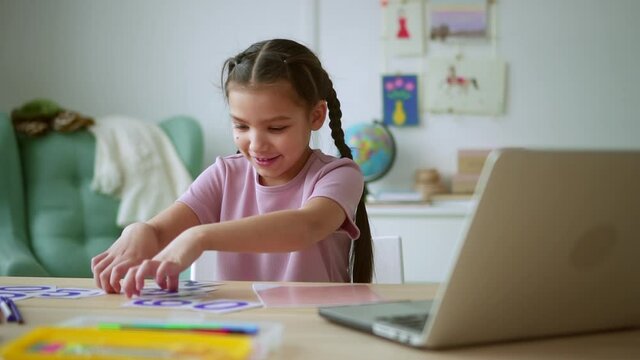 Online primary school education. Spbd Happy little girl with long brown plaits shows card with digit three at distance maths lesson via notebook at home