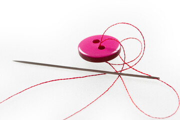 two thread holes, pink button, needle and thread