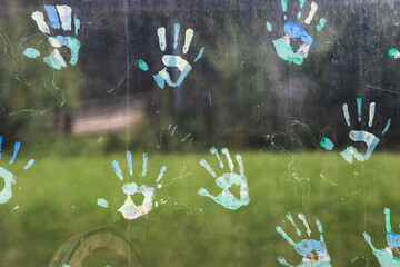 Bunte Handabdrücke aus Fingerfarben auf einer dreckigen Glasscheibe - obrazy, fototapety, plakaty