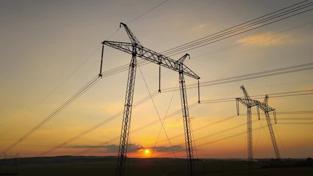 High voltage towers with electric power lines at sunset.