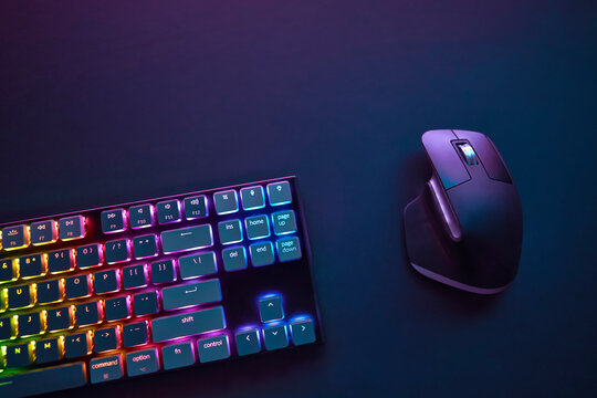 Top down view of vivid color backlighted computer keyboard and mouse against dark background.