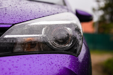 Wet headlight of modern car in violet color on rainy day, close up. Turned off light on vehicle.