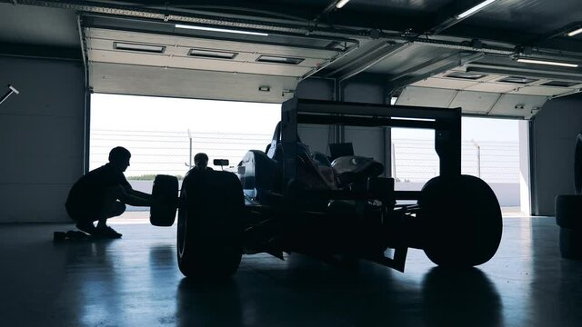 Two men are dismantling a racing car after lifting it