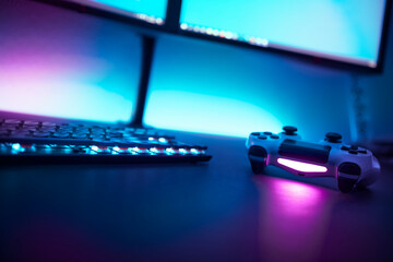Low angle view of backlighted keyboard and game controller on table. Light blue illuminated wall in background.