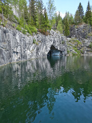 View from the water of the grotto and a section of the flooded Marble Canyon, where trees grow, in the mountain park Ruskeala on a sunny summer day.