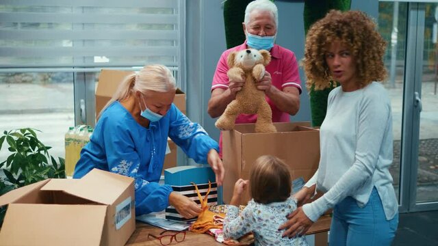 Humanitarian people work at the donation center. A retired old grandfather entertains a little girl by playing with a teddy bear