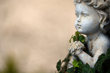 Obraz premium An old, weathered sandstone sculpture of a praying angel who is partially covered with ivy.