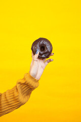 Woman hand holding a chocolate donut against a yellow background
