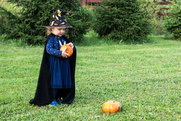 A little girl in a witch costume holds a jack'o ' lantern pumpkin for Halloween. Happy Halloween. A...