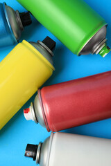 Cans of different graffiti spray paints on light blue background, flat lay