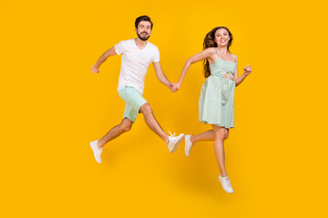 Fototapeta na wymiar Photo of crazy active couple jump hold hands enjoy flight wear casual outfit isolated yellow color background