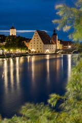 Fototapeta na wymiar Town hall tower of Regensburg and Salzstadel on the banks of the Danube river with Stone Bridge at night