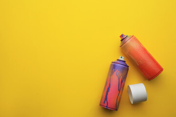 Used cans of spray paints on yellow background, flat lay with space for text. Graffiti supplies