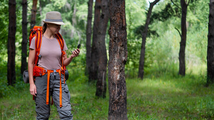 Young caucasian woman is hiking and using a compass in the forest.