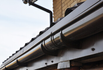 Plastic roof gutter installation with a close-up of a rain gutter joint, joiner, brackets and hangers. Roof gutter repair to prevent water leaks near a joint.