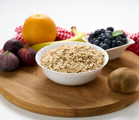 Raw oatmeal in white ceramic plate and fruits on white table, breakfast
