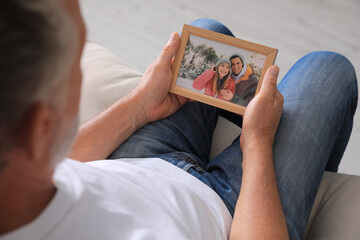 Senior man holding frame with photo of couple at home, closeup