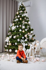 boy in red sweater posing against the background of the christmas tree