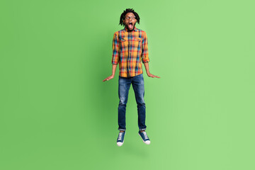 Photo of crazy astonished african guy jump scream open mouth wear plaid shirt jeans isolated green color background