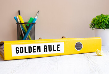 A yellow folder labeled GOLDEN RULE is on the office desk. Flower and stationery background.