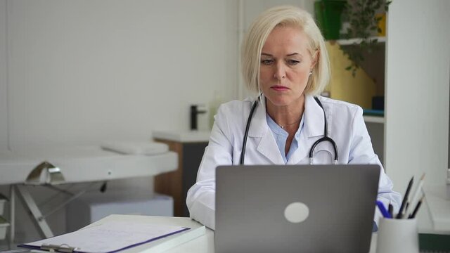 Doctor ehealth online service. Spbd Serious middle-aged female medical worker with stethoscope inputs data from patient history in computer in hospital office