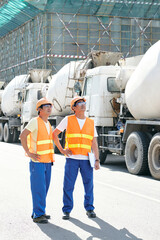 Smiling contractors walking along rows of concrete mixer trucks and planning working day at...